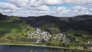 Un piccolo borgo con case raggruppate attorno a un'area centrale, un lago in primo piano e delle colline sullo sfondo.