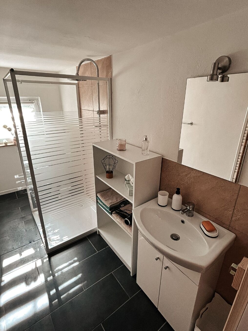 Ein modernes Badezimmer mit einer Duschkabine aus Glas, einem Waschbecken mit Seifenschale und einem Spiegel darüber.
