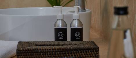 A bathroom with a bathtub, two hand soap bottles, a towel, a woven mat, and a plant.