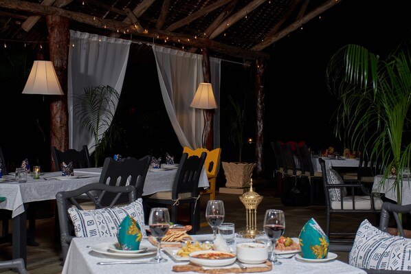 An outdoor dining area with tables set for meals, chairs, and ambient lighting.