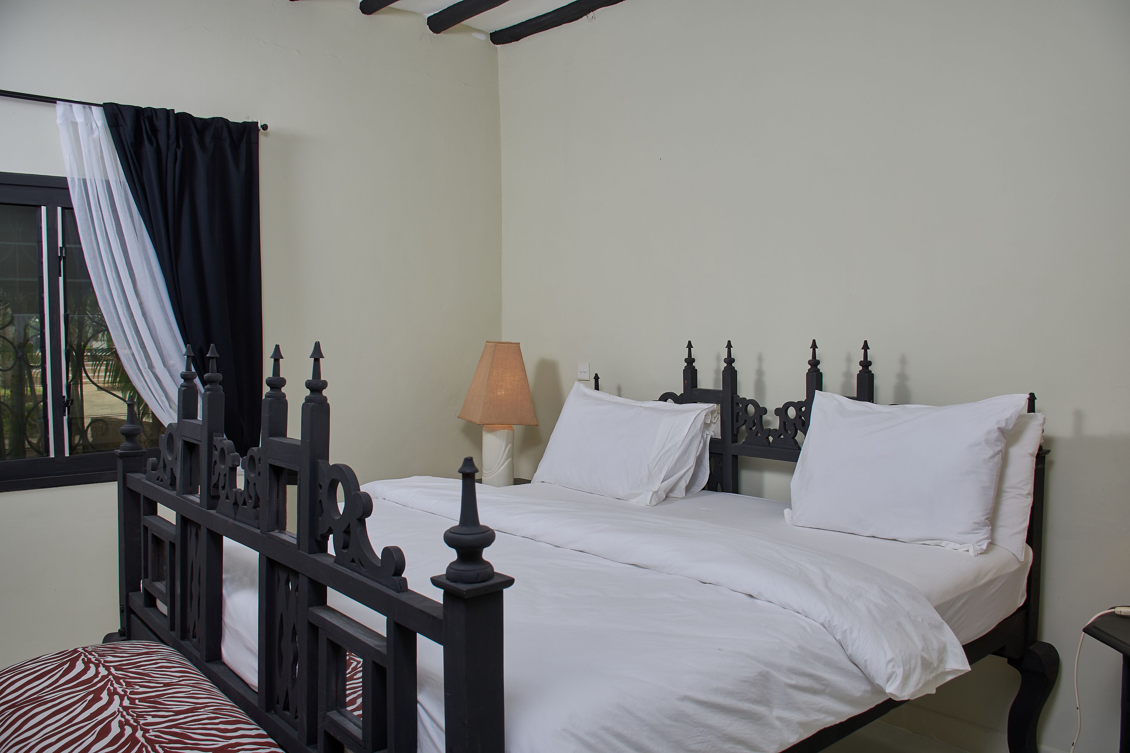 A neatly made bed with a headboard, a bedside lamp, and a window with curtains.