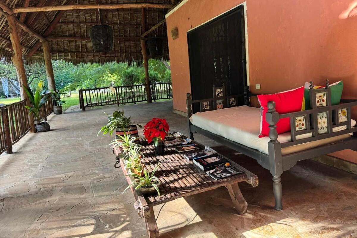 A covered outdoor seating area with a wooden bench and a table with plants and books.