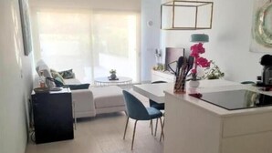 A modern kitchen with a central island, white cabinetry, and a dining area with a blue chair.