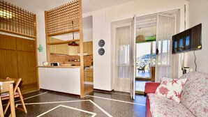 A modern living room with a sofa, a TV, and a kitchen area with wooden cabinets and a dining table.