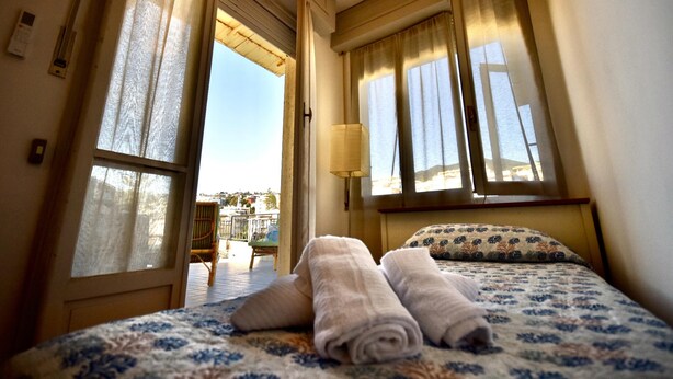 A hotel room with a bed, two rolled towels, a lamp, and a view of the outside.