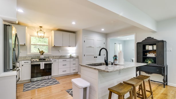 A modern kitchen with white cabinetry, a granite countertop, and a black island with stools. - Relax in a charming cottage near Nelson 151 featuring inviting living spaces and easy access to Virginia's wineries, breweries, hiking trails, and beautiful Blue Ridge scenery. (Afton)