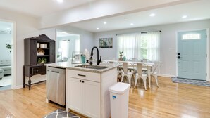 A modern kitchen with white cabinetry, a dishwasher, and a sink. There is a dining area with a white table and chairs. - Relax in a charming cottage near Nelson 151 featuring inviting living spaces and easy access to Virginia's wineries, breweries, hiking trails, and beautiful Blue Ridge scenery. (Afton)