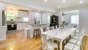 A modern kitchen with white cabinetry, a central island, and a dining area with white chairs. - Relax in a charming cottage near Nelson 151 featuring inviting living spaces and easy access to Virginia's wineries, breweries, hiking trails, and beautiful Blue Ridge scenery. (Afton)