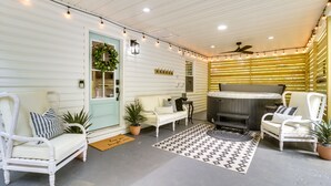 A cozy patio area with a white door, a white sofa, a white armchair, a small table, and a hot tub.