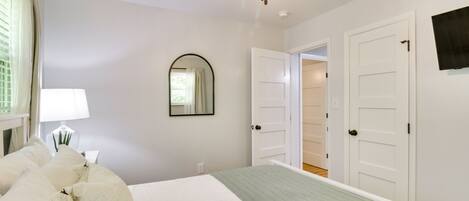 Un dormitorio con cama, ventilador de techo, espejo y puerta que da a otra habitación.