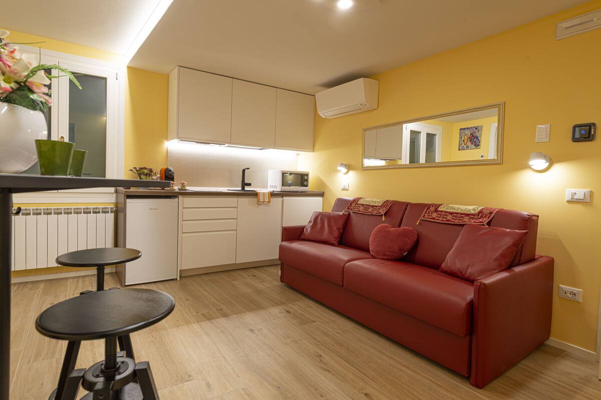 Un espacio habitable compacto con kitchenette, un sofá de cuero rojo y una mesa de comedor con taburetes.