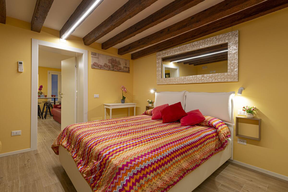 Un dormitorio con cama, mesita de noche, espejo y puerta que da a otra habitación.