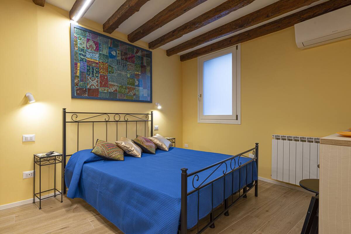 Un dormitorio con cama, mesita de noche, ventana y radiador.