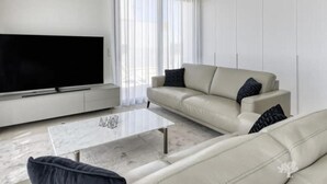 A modern living room with a flat-screen TV, a beige sofa, a coffee table, and a large window with sheer curtains. - Penthouse Limonero 30 (Dehesa de Campoamor)