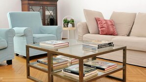 A living room with a light blue armchair, a beige sofa, and a glass coffee table with books. - Treasurerome Spanish Steps Family 4BR (Rome)