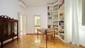 A spacious room with a wooden floor, a wooden desk, a chair, and a large white bookshelf filled with books. - Treasurerome Spanish Steps Family 4BR (Rome)