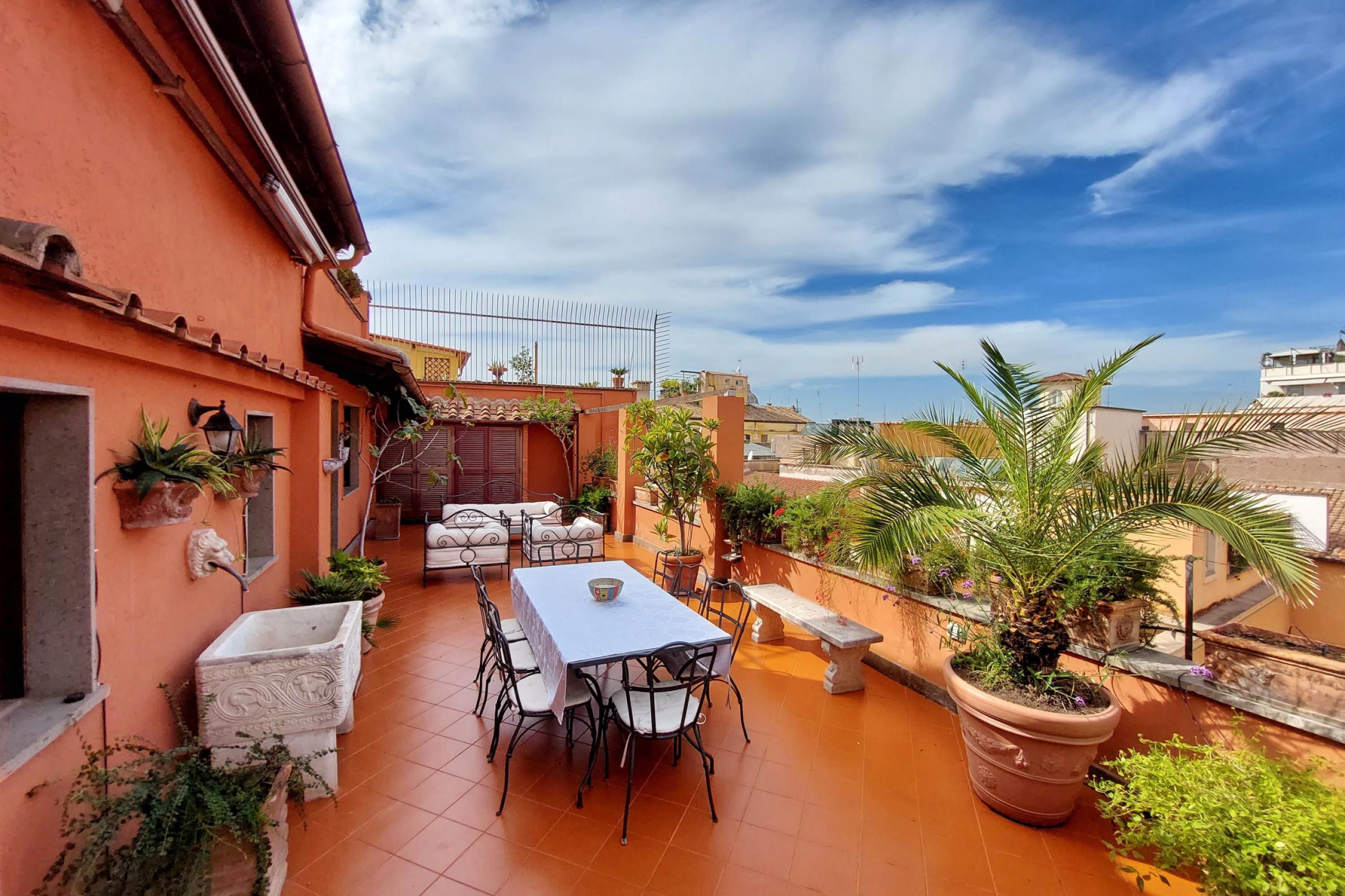 A patio with a table and chairs, surrounded by potted plants and a railing.