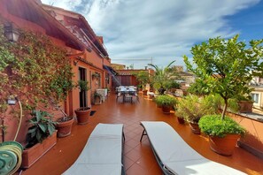 Terraço no telhado com área de jantar, plantas em vasos e duas cadeiras de descanso.