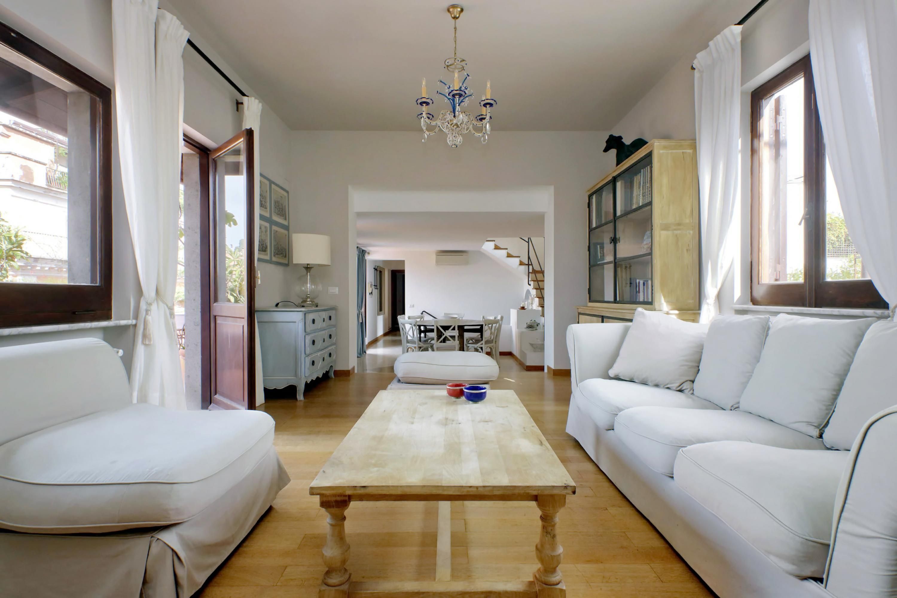 A spacious living room with a wooden coffee table, white sofas, and a chandelier.