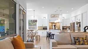 A modern kitchen with white cabinets, a central island, and a dining area with a table and chairs. - All Inclusive  Super Mario Hideout Arcade PIckleball Pool Slide (Indio)
