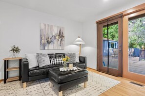 A modern living room with a black leather sofa, a white rug, a floor lamp, and a cityscape painting. - Charming and Spacious House with Relaxing Huge Deck (Kirkland)