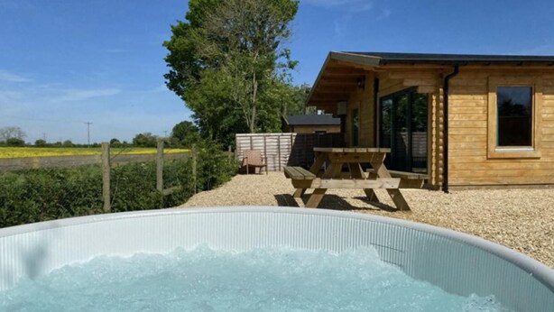 A wooden cabin with a hot tub, picnic table, and a view of the countryside. - Inviting 2-bedroom Cabin in Ashton Under Hill (Evesham)