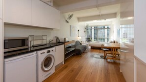 A modern kitchen with a washing machine, microwave, and a dining area with a table and chairs. - Central Studio in the Heart of Melbourne Cbd! (Melbourne)