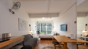 A modern, well-lit room with a wooden floor, a bed, a desk, a chair, a table, and a fan. - Central Studio in the Heart of Melbourne Cbd! (Melbourne)