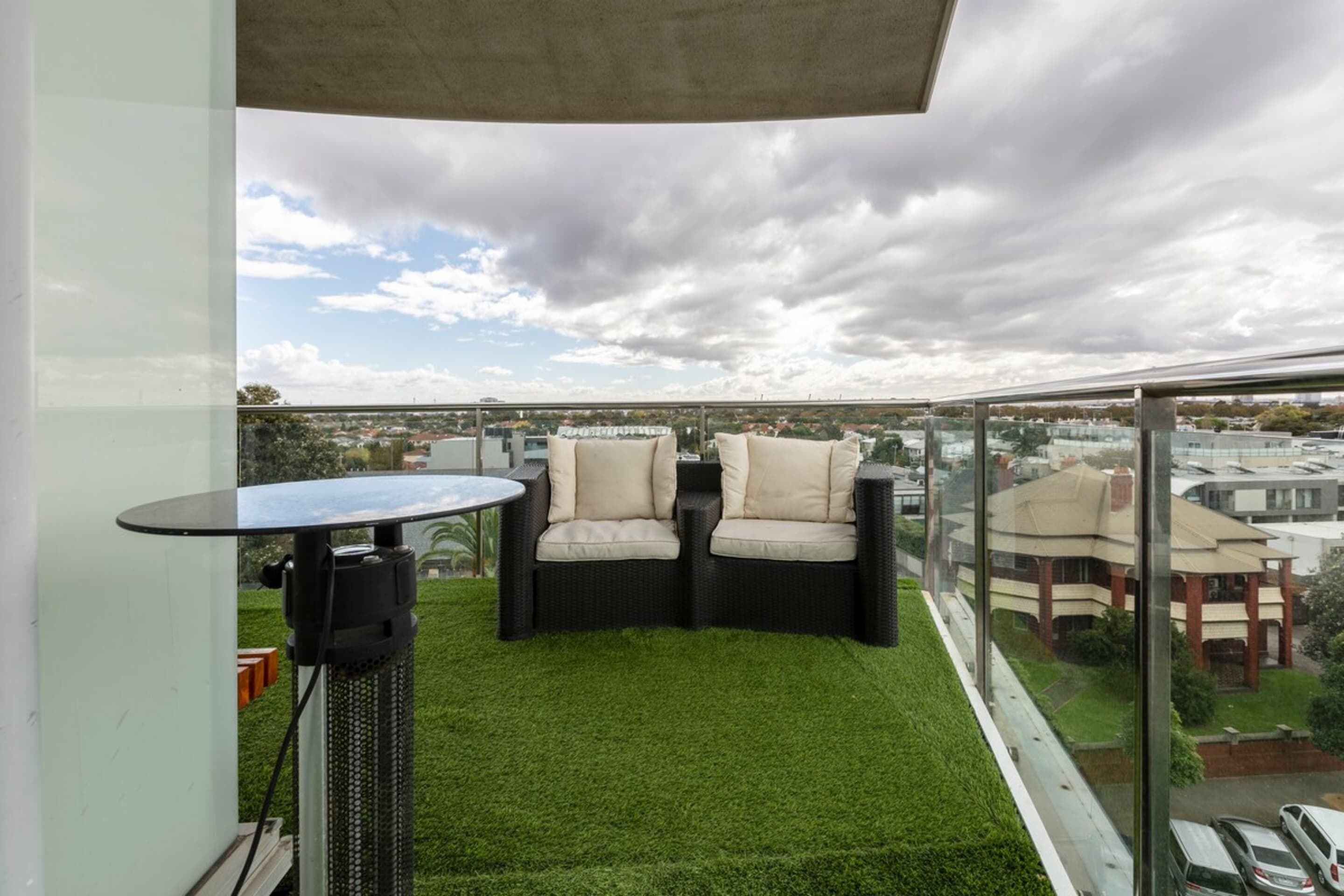 A balcony with a glass railing, a round table, two cushioned chairs, and a small speaker.