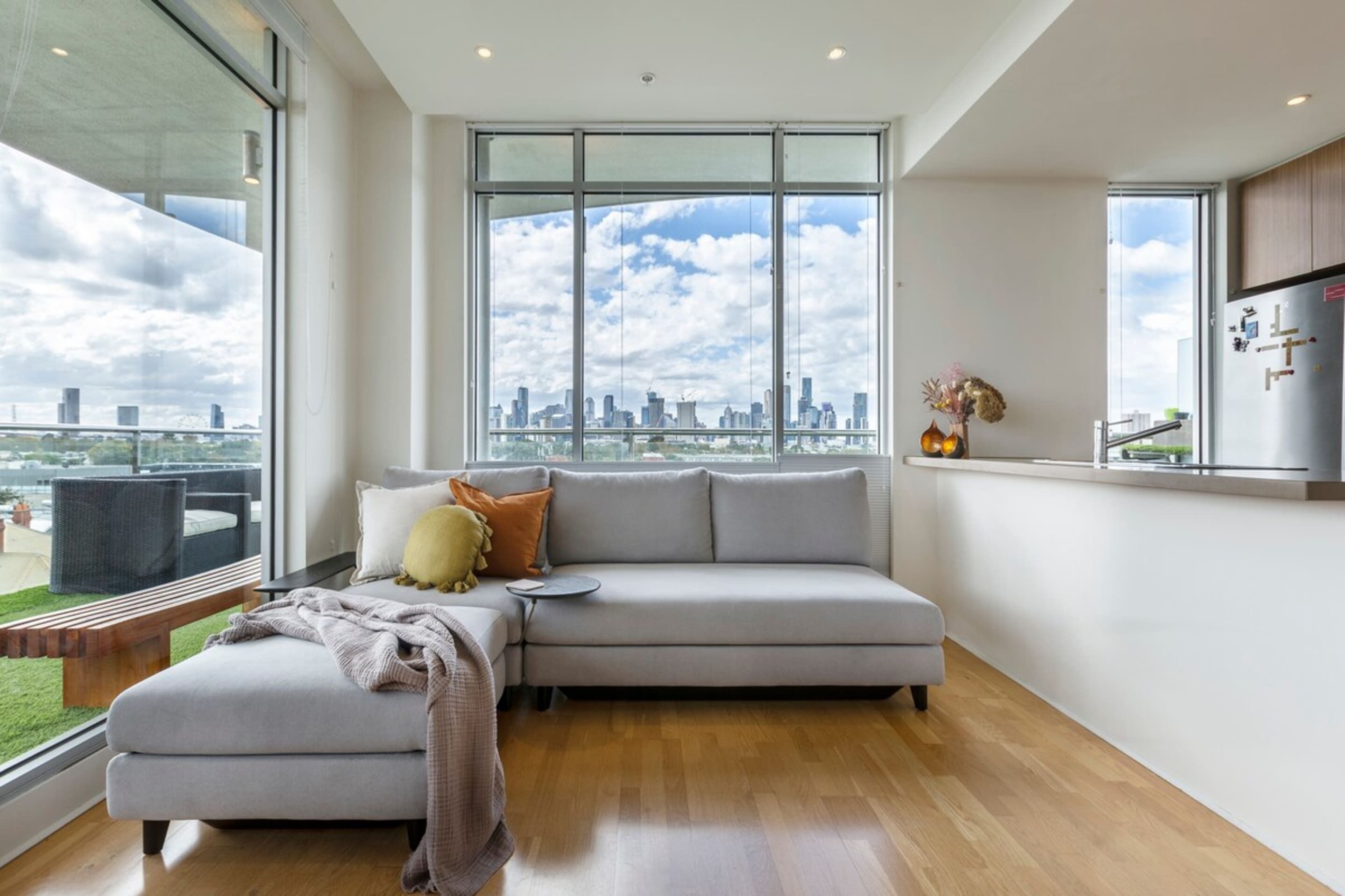 A modern living room with a large window, a grey sofa, a small table, and a wooden bench.