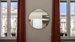 A room with a large window, a round mirror on the wall, and a view of a building with classical architecture. - Trastevere 143 (Rome)