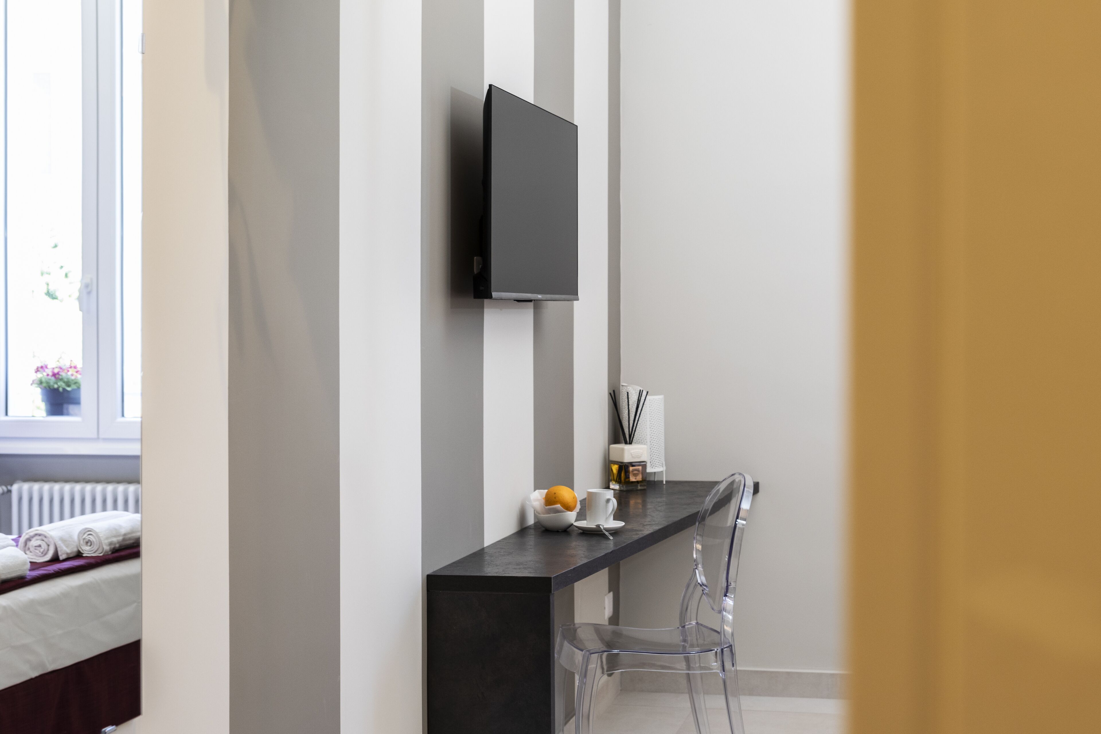 Un baño moderno con encimera negra, televisor montado y una silla transparente.