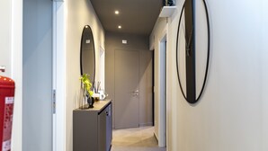 A narrow hallway with a door at the end, a fire extinguisher on the left, and a mirror on the right wall. - Trastevere 143 (Rome)