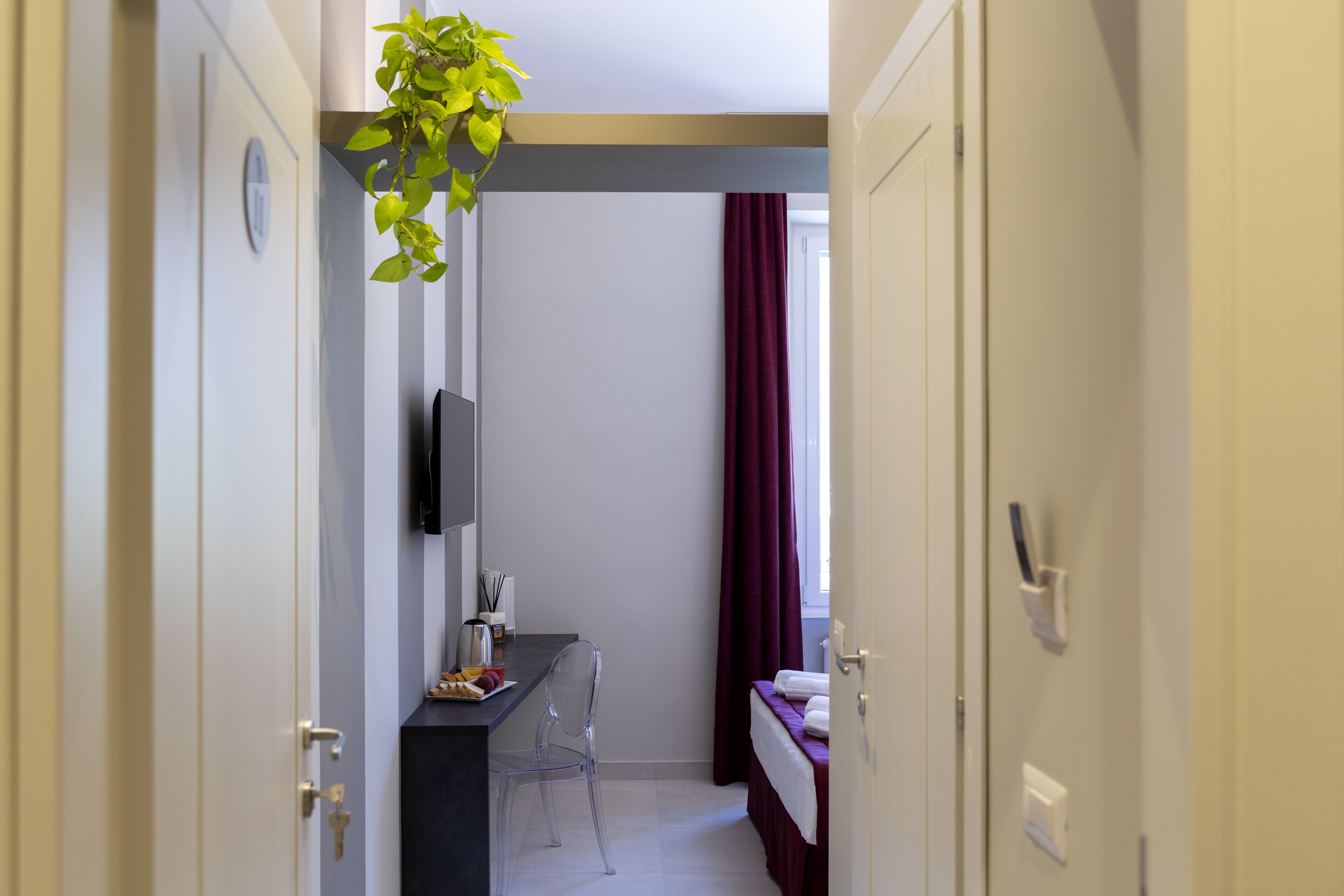 A narrow hallway with a bed, a desk, and a TV on the wall.