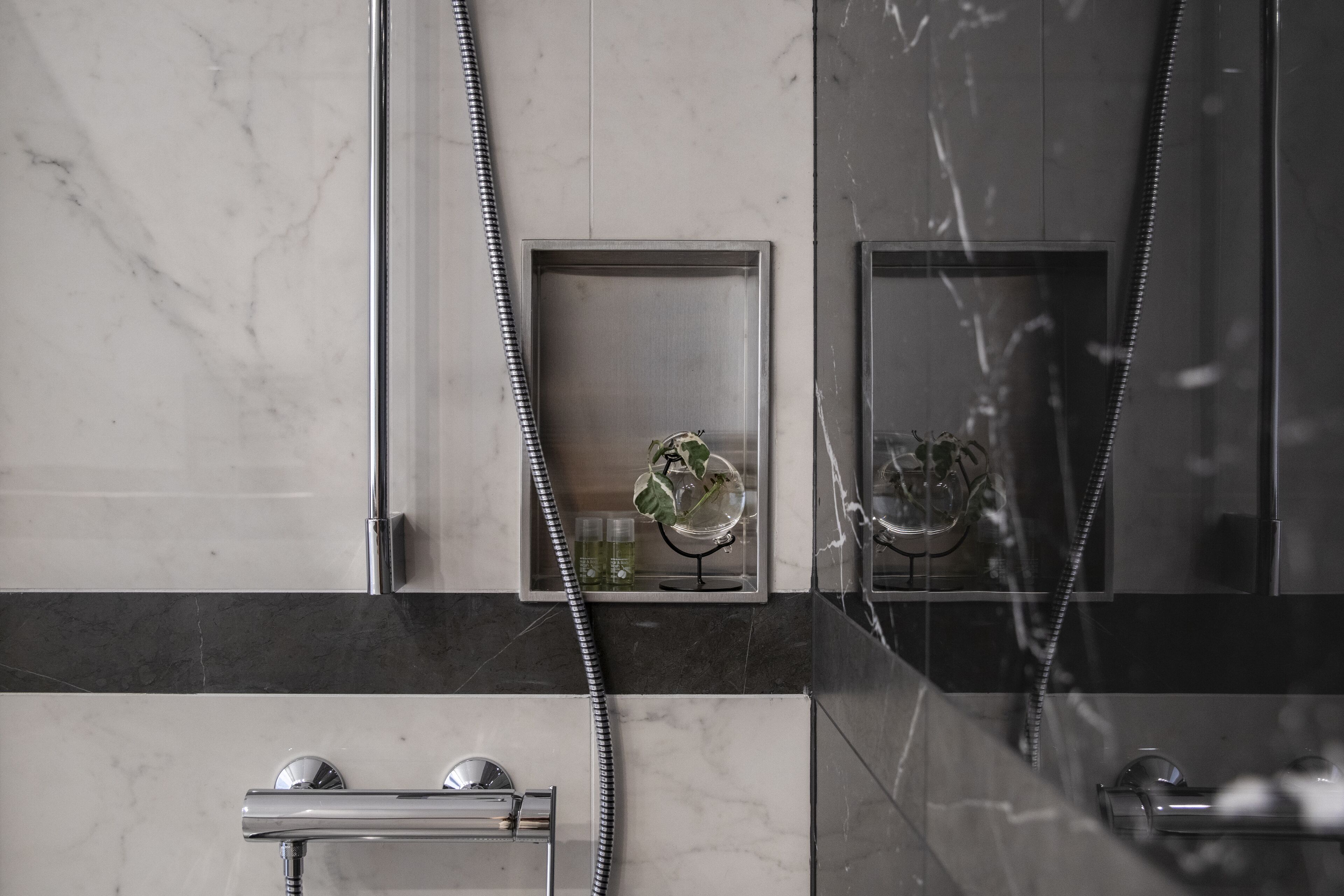 Een moderne badkamer met een douche, een glazen plankje met toiletartikelen en een marmeren wand.