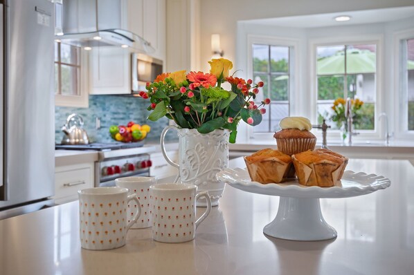 A kitchen with a white countertop, a decorative pitcher with flowers, and a plate of pastries.