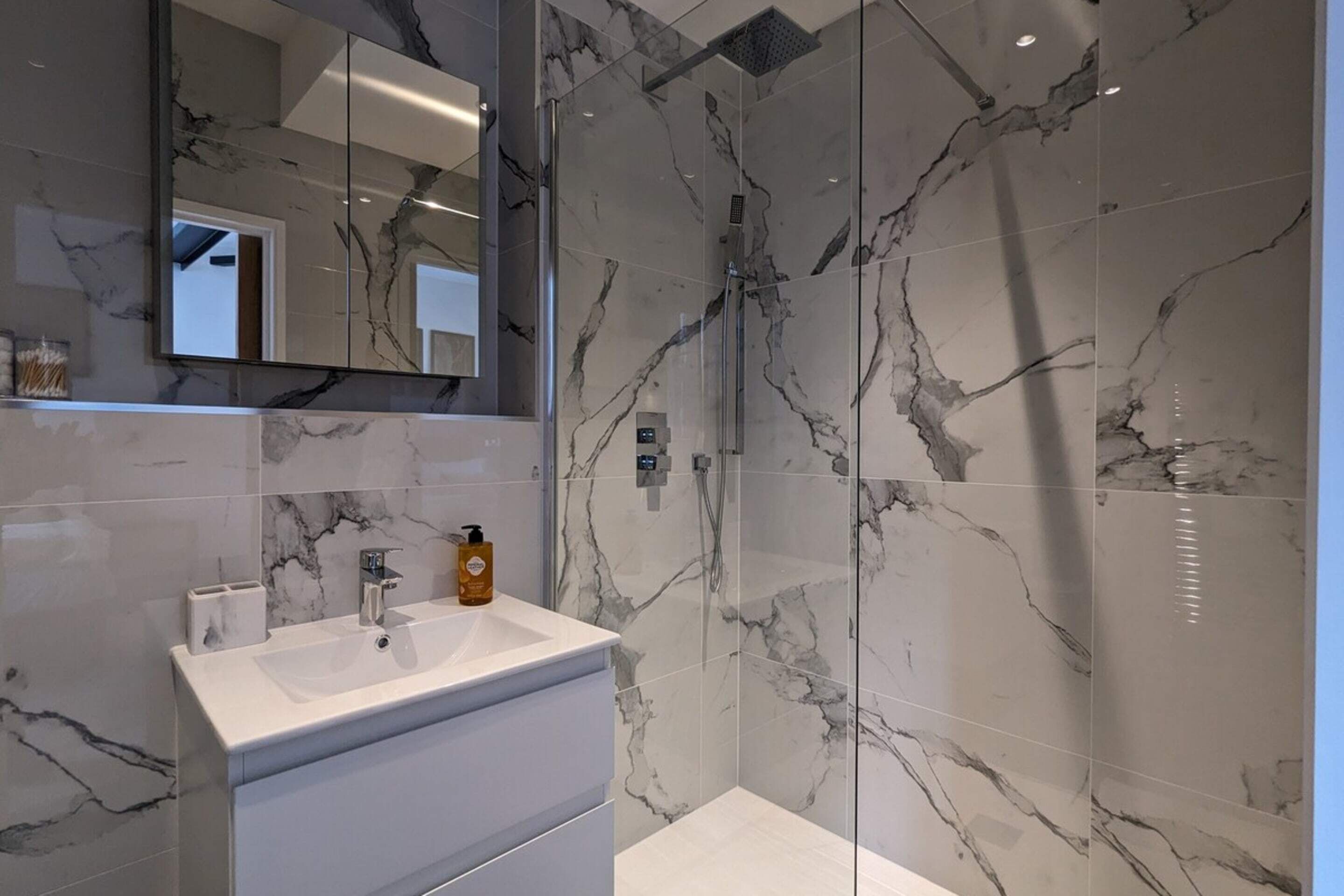A modern bathroom with a marble shower, a large mirror, and a white vanity with a sink.