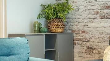 A room with a grey sofa, a blue armchair, a wicker plant pot, and a brick wall.