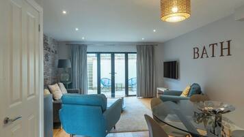 A modern living room with a glass dining table, blue sofas, and a 'BATH' sign on the wall.