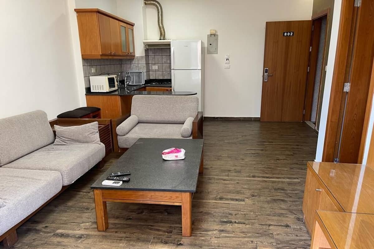 A compact living space with a sofa, a small table, a kitchenette, and a wooden door marked with the number 802.