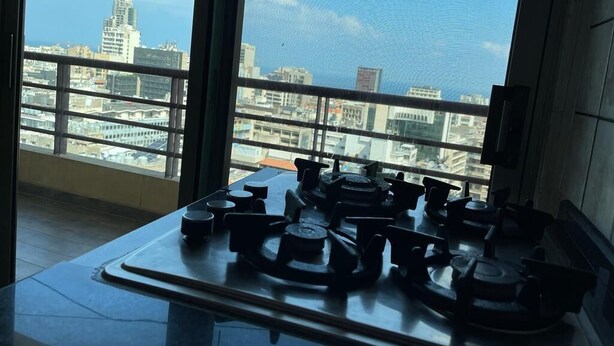 A kitchen with a gas stove and a view of a cityscape through large windows. - New Home Residence (Beirut)