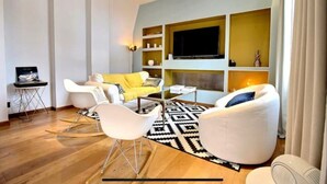 A modern living room with a yellow sofa, white armchairs, a black and white rug, and a flat-screen TV mounted on a wall. - Appartement Design Rouen-gare Parking-netflix, 3 Chambres, 2 Salles de Bains (Rouen)