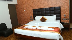 A hotel room with a brick wall, a black upholstered headboard, a bed with white bedding, and a swan-shaped towel arrangement. - Hotel Merlin Interantional (Thrissur)