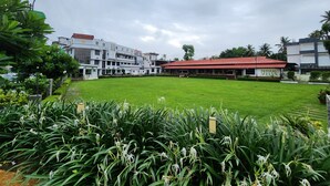A hotel with a large lawn, a red-roofed building, and a sign reading "PANDHAL". - Hotel Merlin Interantional (Thrissur)
