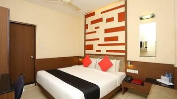 A hotel room with a bed, a desk, a chair, a nightstand, a mirror, and a ceiling fan.