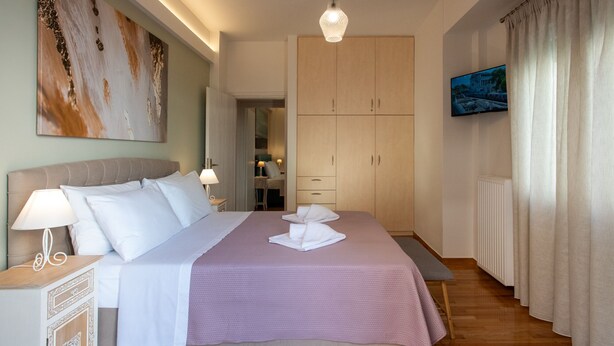 Quarto bem arrumado com cama, mesas de cabeceira, guarda-roupa e televisão.