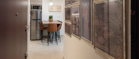 A hallway leading to a kitchen with a dining area, featuring framed pictures on the wall.