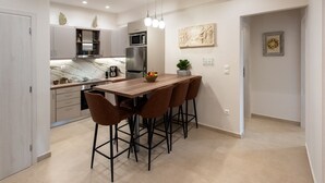 Uma cozinha moderna com bancada de mármore, eletrodomésticos de aço inoxidável e uma mesa de jantar de madeira com quatro cadeiras.
