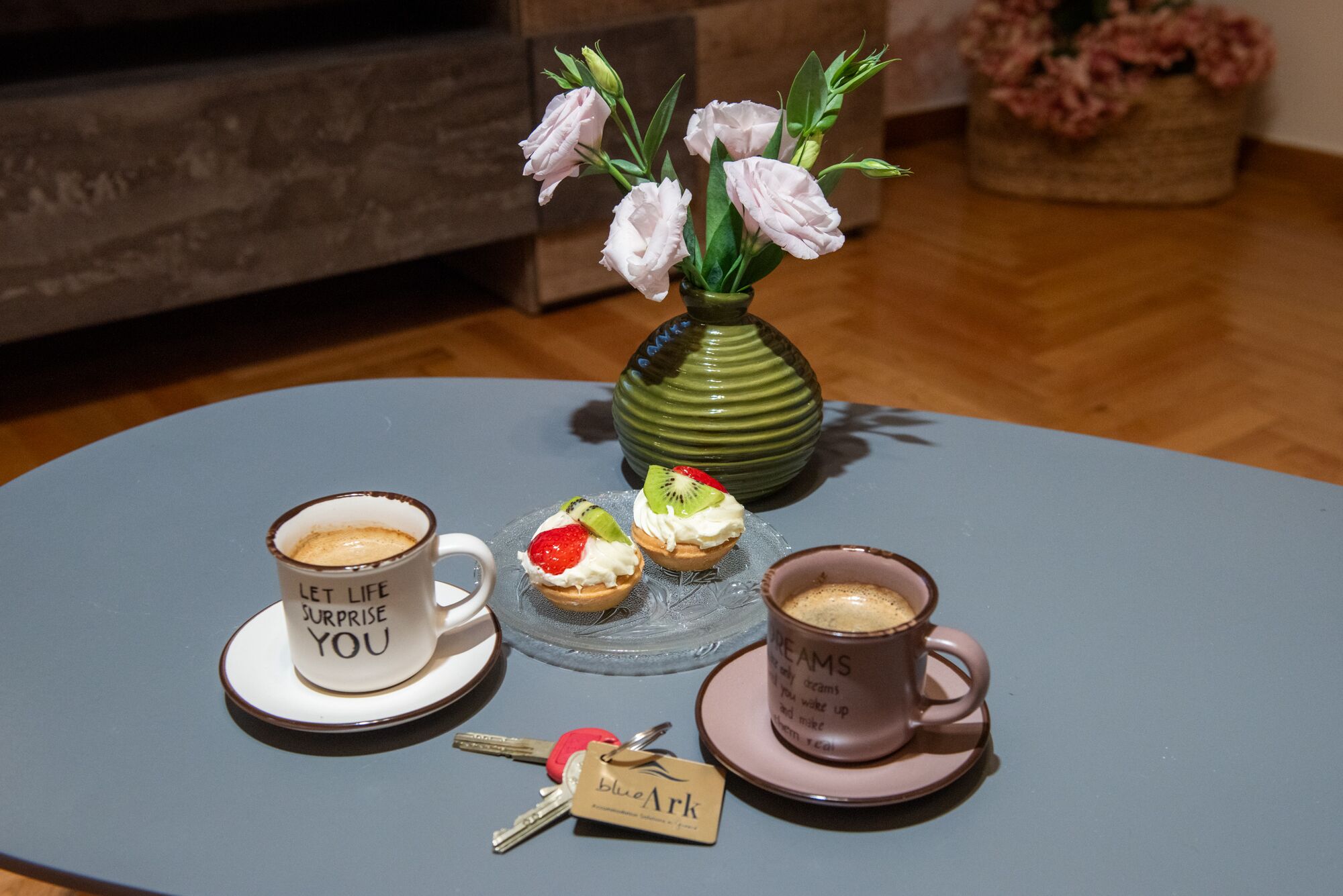 A table with three cups of coffee, a vase with flowers, and a keychain with a name tag.