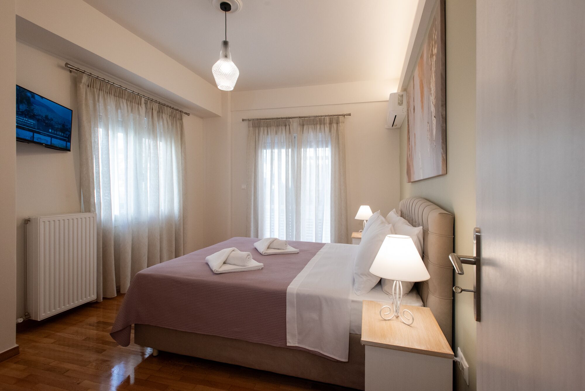 Una habitación de hotel con cama, mesita de noche con lámpara, radiador y cortinas.